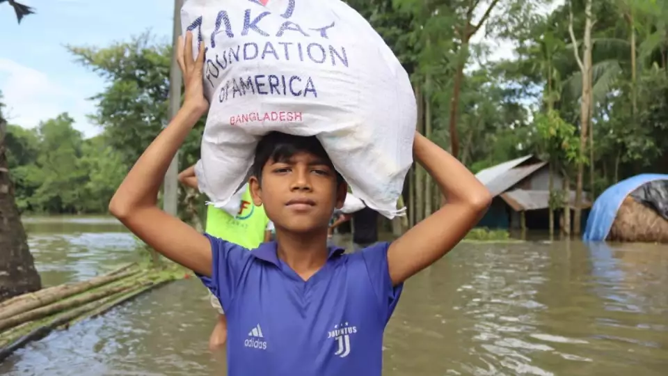 A Bangladeshi child holds our relief package as he wades through flood waters.